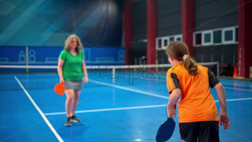 Video A woman and a child training to play pickleball on a blue, inside court - Starpik Stock