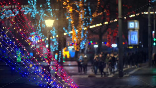 Video Close up of colourful Christmas lights sparking with a blurry view of people crossing the street in the background - Starpik Stock