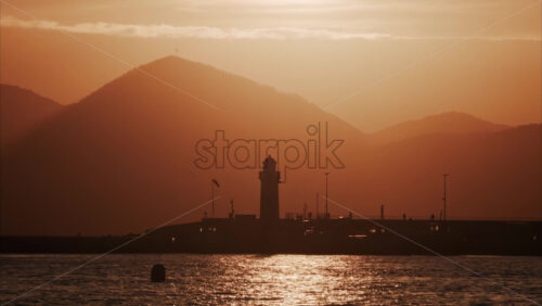 Video Distant view of a lighthouse with the mountains on the background at sunset - Starpik Stock