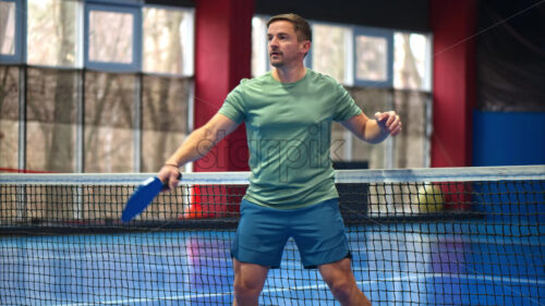 Video Man in a green shirt playing pickleball on a blue, inside court - Starpik