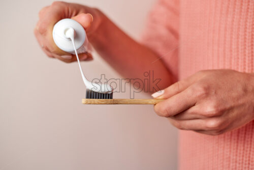 Woman hands squeezing toothpaste on bamboo. Wearing pink knitted sweater - Starpik