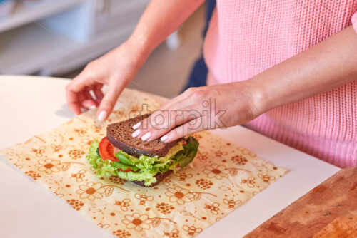 Woman hands wrapping a healthy sandwich in beeswax food wrap. Fruits in shallow focus on background. Bananas and apples. Place for text - Starpik