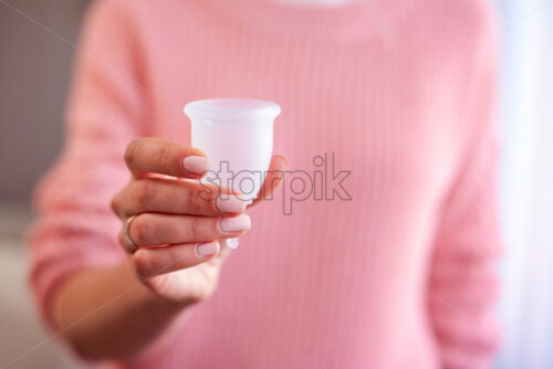 Woman holding in hands menstrual cup. Wearing pink knitted sweater at home - Starpik