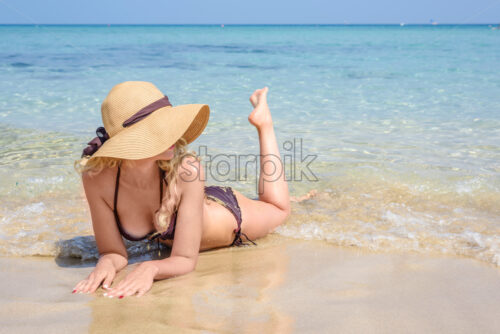 Woman laying on the beach in Cyprus. Hat and swimsuite. Beautiful Summer seaside views. Enjoying sunny day - Starpik