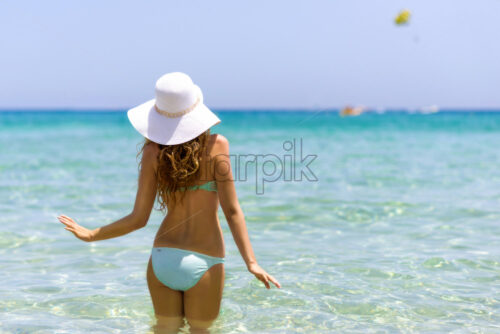 Young woman at the beach. Portrait of a girl in white hat having fun in the water. Beautiful Summer sea with turquoise water. View from behind, cyprus island - Starpik