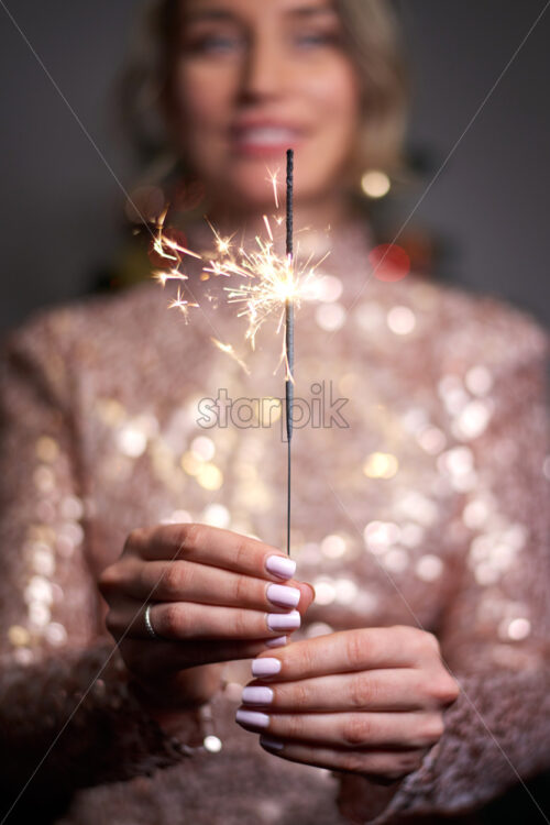 Young woman holding sparkler and smiling. Wearing shiny dress. Christmas holiday idea - Starpik