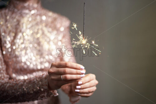 Young woman holding sparkler in hands. Wearing shiny dress. Christmas holiday idea - Starpik