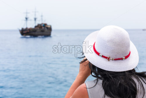 Young woman watching a boat with binoculars from far distance. Blurred background - Starpik